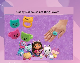 Puede incluir: Un conjunto de anillos de regalo de gato coloridos con los personajes de la casa de muñecas de Gabby. Los anillos están hechos de plástico suave y presentan gatos de diferentes colores con caras sonrientes. Los anillos son perfectos para una fiesta con el tema de la casa de muñecas de Gabby.