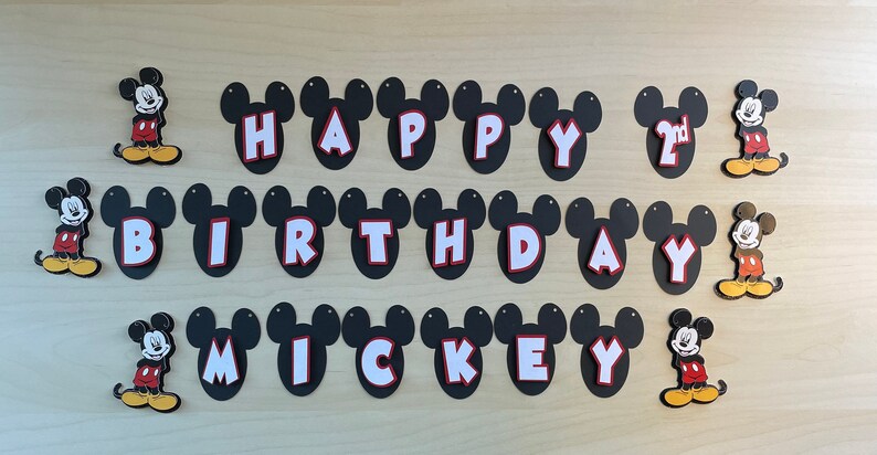 May include: A black and white Mickey Mouse themed birthday banner with the words "Happy 2nd Birthday Mickey" in white letters with red outlines. The banner is decorated with Mickey Mouse heads and figures.