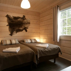 Könnte beinhalten: Zwei Einzelbetten mit braunen Bettdecken und weißen Handtüchern in einer Holzhütte mit einer großen Tierhaut an der Wand.
