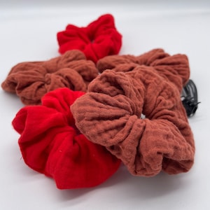Könnte beinhalten: Ein Set mit fünf Haargummis in Rot und Braun. Die Haargummis sind aus einem weichen, strukturierten Stoff.
