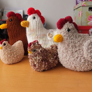 May include: Five crocheted chicken toys in various colors, including brown, white, beige, and brown with red accents. The chickens are all sitting on a wooden surface.