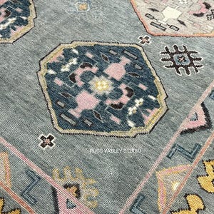 Puede incluir: Una alfombra azul con un patr&oacute;n geom&eacute;trico en tonos de rosa, amarillo y azul. La alfombra tiene un borde con un patr&oacute;n repetitivo de tri&aacute;ngulos y cuadrados.