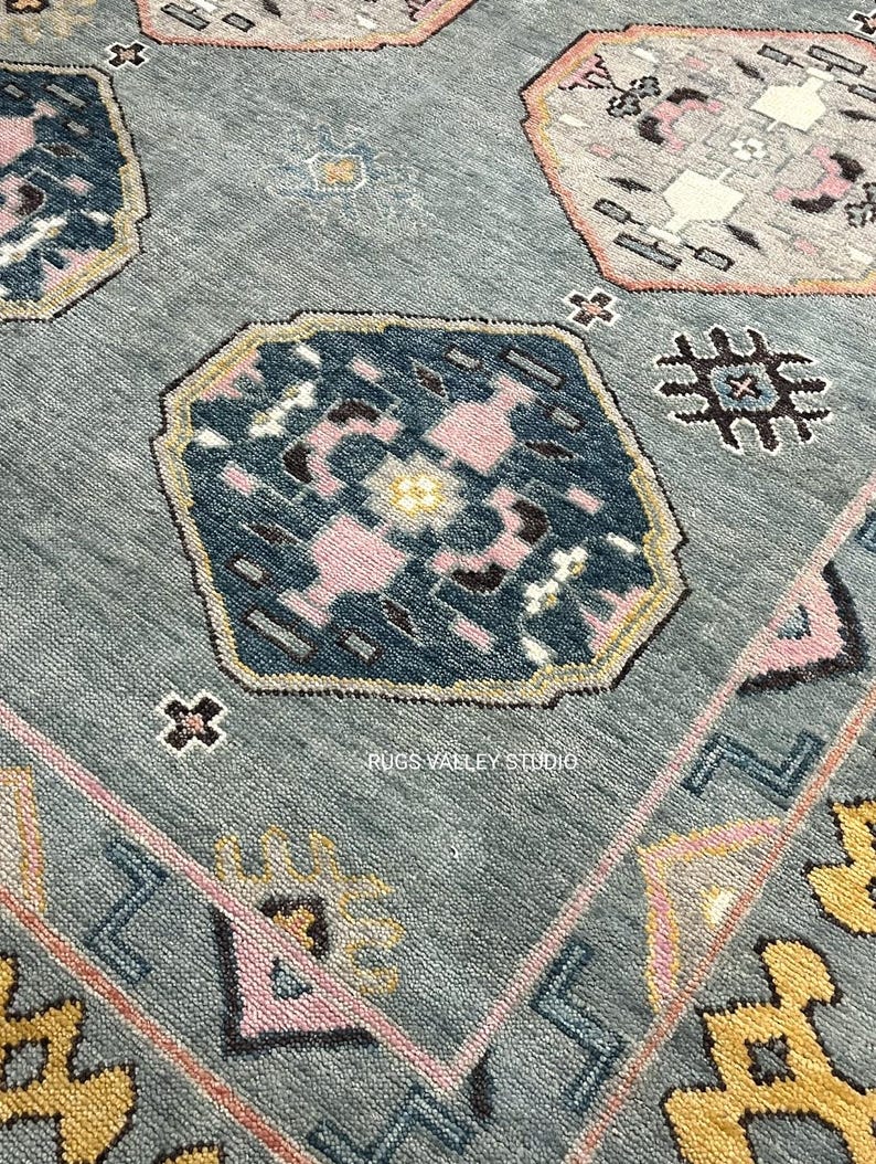 Puede incluir: Una alfombra azul con un patr&oacute;n geom&eacute;trico en tonos de rosa, amarillo y azul. La alfombra tiene un borde con un patr&oacute;n repetitivo de tri&aacute;ngulos y cuadrados.