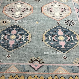 Puede incluir: Una alfombra azul y rosa con un dise&ntilde;o geom&eacute;trico. La alfombra tiene un borde amarillo y dorado.