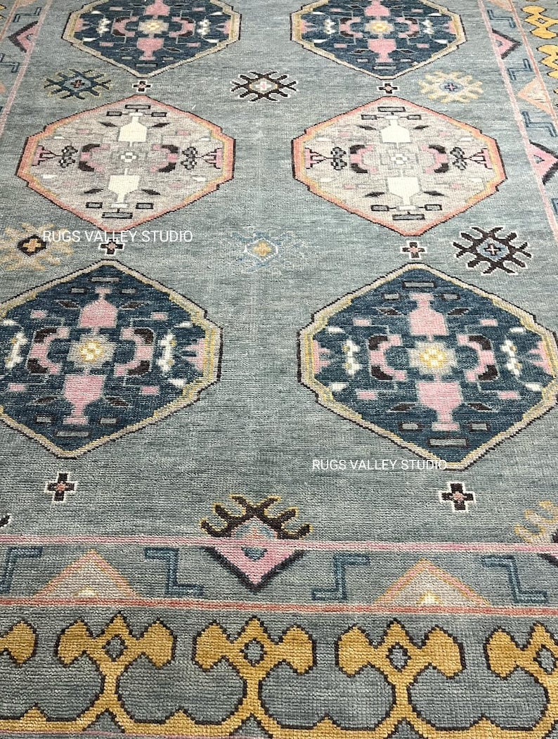 Puede incluir: Una alfombra azul y rosa con un dise&ntilde;o geom&eacute;trico. La alfombra tiene un borde amarillo y dorado.
