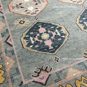 Puede incluir: Una alfombra azul con un patr&oacute;n geom&eacute;trico en tonos de rosa, amarillo y marr&oacute;n. La alfombra tiene un borde amarillo y rosa. El texto "RUGS VALLEY STUDIO" aparece dos veces en la alfombra.