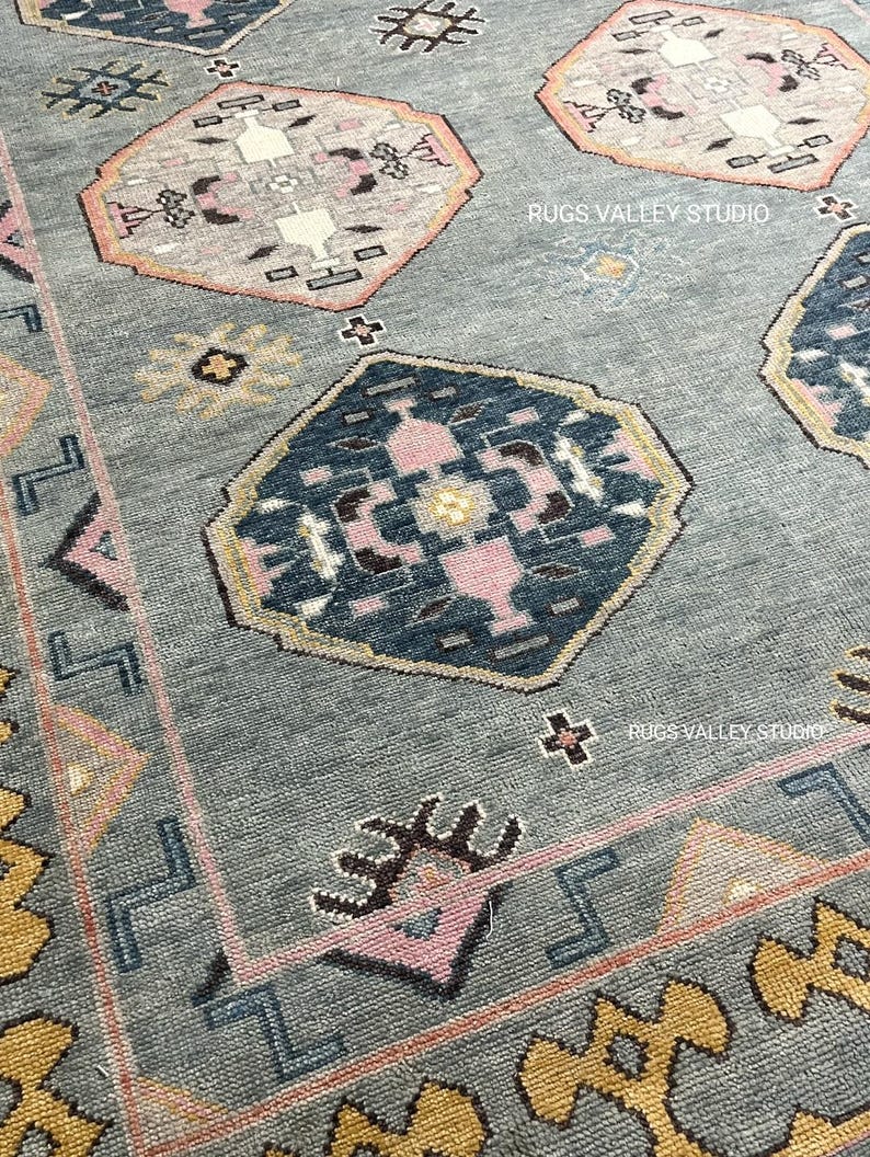 Puede incluir: Una alfombra azul con un patr&oacute;n geom&eacute;trico en tonos de rosa, amarillo y marr&oacute;n. La alfombra tiene un borde amarillo y rosa. El texto "RUGS VALLEY STUDIO" aparece dos veces en la alfombra.