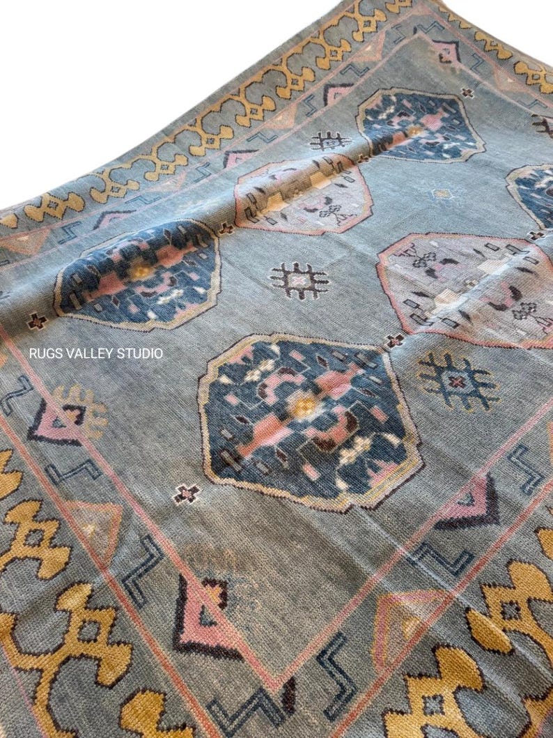Puede incluir: Una alfombra vintage con fondo azul y patrones intrincados en tonos de rosa, amarillo y azul. La alfombra tiene un dise&ntilde;o geom&eacute;trico con un medall&oacute;n central y un borde.
