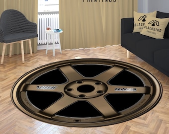 May include: A round brown and black car wheel rug with the text "RAYS" and "VOLK" on it. The rug is on a wood floor in a living room setting.