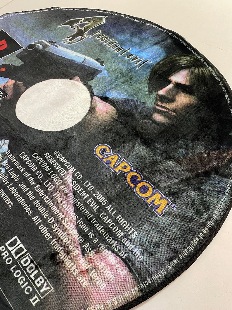 May include: A Resident Evil PlayStation 2 game disc featuring a character holding a gun. The disc has the Capcom logo and the text "Resident Evil" in a stylized font. The disc is black, blue, and white.