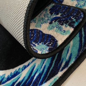 K&ouml;nnte beinhalten: Ein schwarzer und blauer Teppich mit Wellenmuster. Der Teppich hat einen schwarzen Rand und einen wei&szlig;en Hintergrund.