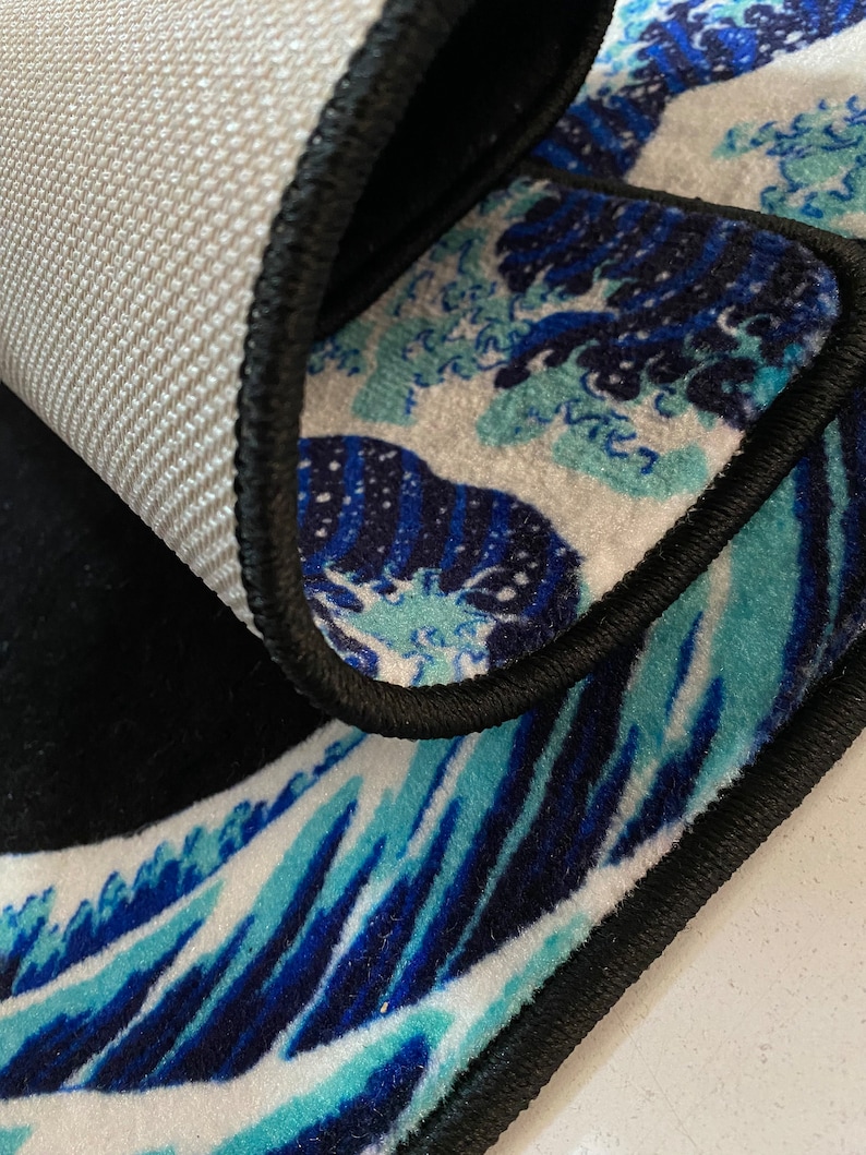 K&ouml;nnte beinhalten: Ein schwarzer und blauer Teppich mit Wellenmuster. Der Teppich hat einen schwarzen Rand und einen wei&szlig;en Hintergrund.