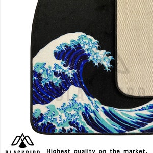 K&ouml;nnte beinhalten: Eine schwarze Autofu&szlig;matte mit einem blauen und wei&szlig;en Wellendesign. Die Matte hat eine rutschfeste R&uuml;ckseite.