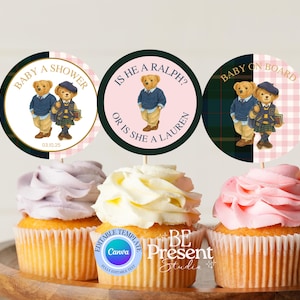 May include: Cupcake toppers for a baby shower, with teddy bears in smart outfits. The toppers say "Baby a Shower", "Is he a Ralph? or is she a Lauren?" and "Baby on Board". The cupcakes have purple, white, and pink icing.