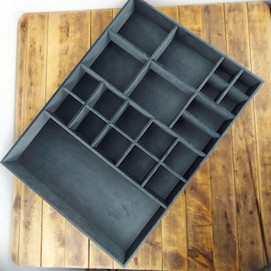 May include: A gray velvet-lined jewelry organizer with multiple compartments of varying sizes. The organizer is rectangular and has a smooth, flat surface.