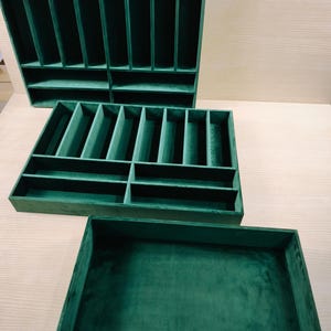May include: Three rectangular dark green velvet-lined storage trays. Two trays feature multiple vertical and horizontal dividers creating various compartments for organization, while the third tray is an open, undivided rectangular container.