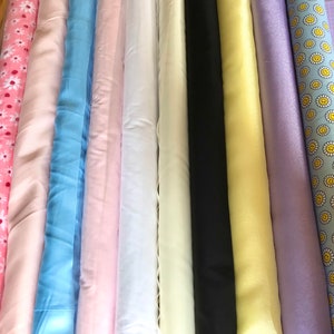 May include: A collection of fabric rolls in various colours and patterns, including pink, blue, white, yellow, and purple. Some fabrics have a floral pattern, while others are solid colours.