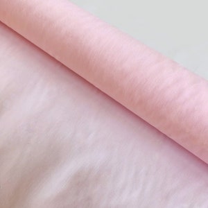 May include: A roll of pale pink tissue paper. The paper is soft and delicate, perfect for wrapping gifts or creating crafts.