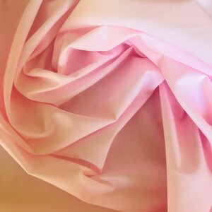 May include: A close-up of a soft, pink fabric with a smooth texture. The fabric is folded and draped, creating a delicate and flowing look.