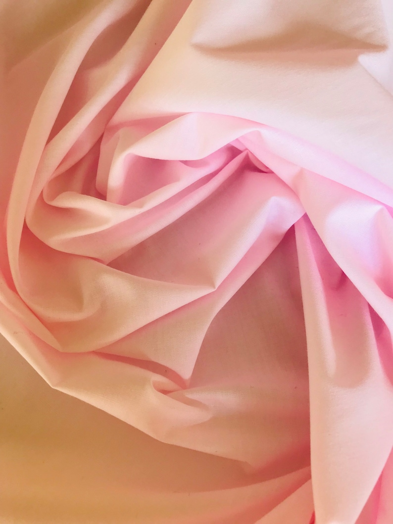 May include: A close-up of a soft, pink fabric with a smooth texture. The fabric is folded and draped, creating a delicate and flowing look.