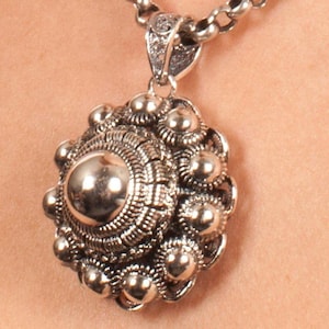 May include: A silver pendant necklace with a round, ornate design. The pendant is made of many small, round beads and has a textured surface.