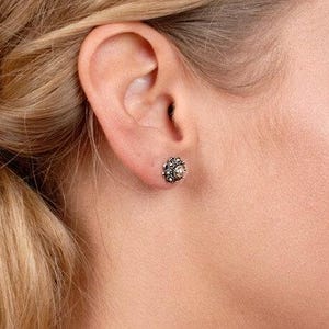 May include: A close-up of a person's ear wearing a small silver stud earring with a round, textured design.