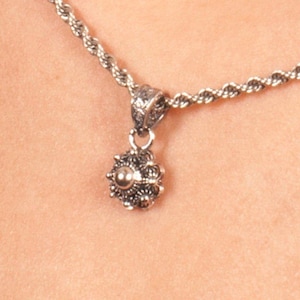 May include: A silver chain necklace with a silver pendant featuring a detailed floral design.