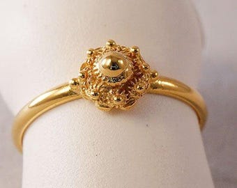 May include: A gold ring with a detailed, ornate design. The ring features a central round shape surrounded by intricate floral patterns.