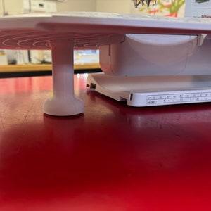 May include: White sewing machine with a white extension table and a white foot pedal. The table has a ruler with markings in inches and centimeters.