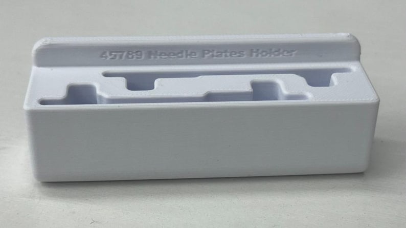 Peut inclure: Porte-plaques d'aiguilles en plastique blanc avec le texte "45789 Needle Plates Holder" imprim&eacute; sur le dessus.