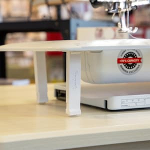 May include: White sewing machine with a white extension table and two white legs. The machine has a sticker that says "170% Capacity, Bernina Exclusive".