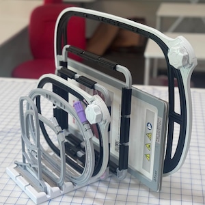 May include: A medical device with a white and black handle and frame, holding several rectangular components. The device has a complex design with curved and straight lines, and a white base. The components include a purple tube and a white knob.
