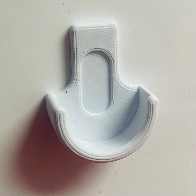 Op de afbeelding: Witte plastic wandbevestiging met een gebogen, open ontwerp. De bevestigin is ontworpen om een rond object te houden.