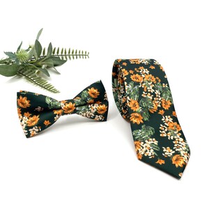 Peut inclure: Une cravate vert fonc&eacute; et un n&oelig;ud papillon assorti, tous deux orn&eacute;s d'un motif r&eacute;p&eacute;titif de fleurs orange, de petites fleurs blanches et de feuilles vertes. L'ensemble est pr&eacute;sent&eacute; avec un petit brin de feuillage vert sur fond blanc.