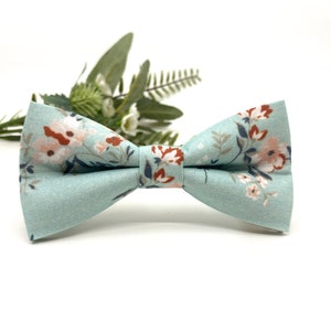 May include: A light blue bow tie with a floral pattern in shades of pink, orange, and white.