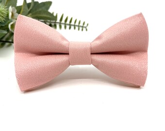 May include: A light pink bow tie with a subtle shimmer finish. The bow tie is made of a soft, textured fabric.