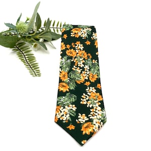 Peut inclure: Une cravate pr&eacute;sentant un fond vert for&ecirc;t fonc&eacute; avec un motif floral r&eacute;p&eacute;titif de fleurs orange vif et de fleurs blanches entrem&ecirc;l&eacute;es de feuilles vertes. Le tissu a une texture visible et une extr&eacute;mit&eacute; pointue sur la partie inf&eacute;rieure.