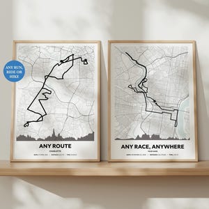 Puede incluir: Dos impresiones enmarcadas de mapas en una estantería de madera. La impresión de la izquierda tiene una ruta negra sobre un mapa de la ciudad con el texto "ANY ROUTE" y "CHARLOTTE". La impresión de la derecha tiene una ruta negra con el texto "ANY RACE, ANYWHERE". Un círculo azul dice "ANY RUN, RIDE OR HIKE".