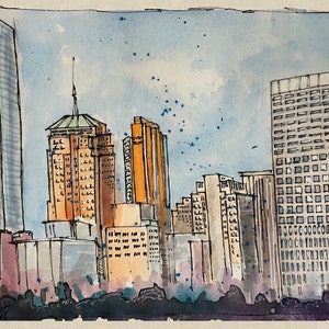 May include: Watercolor painting of a city skyline with tall buildings. The buildings are in shades of gray, orange, and tan, with a blue sky and blue paint splatters. The artist's signature is in the bottom left corner.