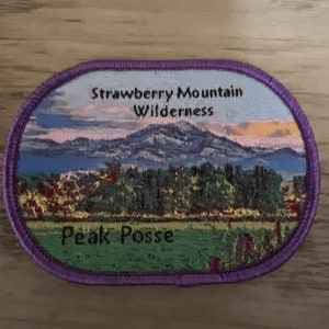 May include: Purple oval-shaped patch with a scenic image of a mountain range with a sunrise in the background. The text "Strawberry Mountain Wilderness" is at the top of the patch and "Peak Posse" is at the bottom.