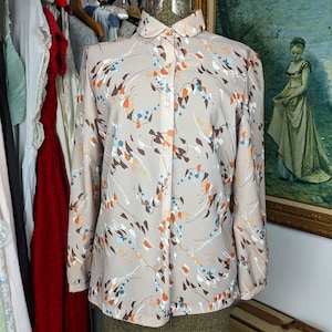 May include: A beige long-sleeved blouse with a white collar and a brown, orange, and blue abstract print.