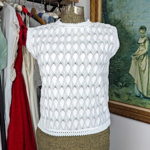 May include: White crochet top with a diamond pattern. The top is sleeveless and has a scalloped hem.