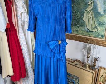 May include: A royal blue pleated dress with a matching satin skirt and a large satin bow at the waist. The dress has a scoop neckline and short sleeves.