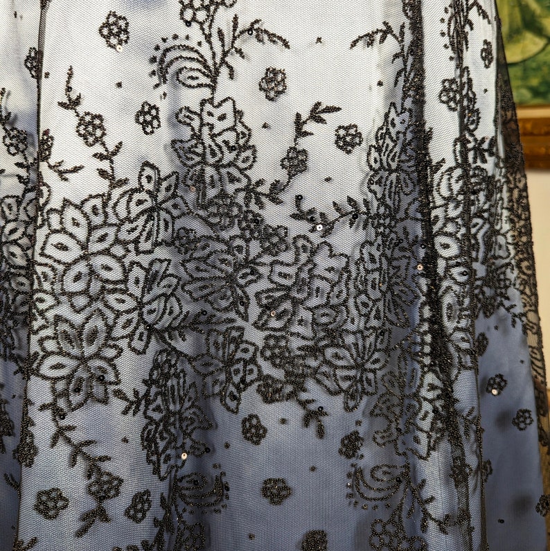 May include: Black floral lace fabric with a delicate pattern. The lace is on a sheer, light blue background.