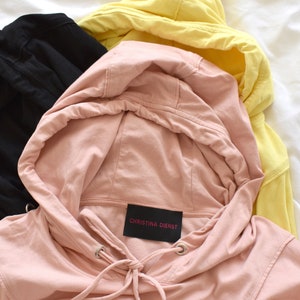 Light pink hoodie in lightweight t-shirt cotton, tonal piping along sleeves and chest, drawstring with silver endings