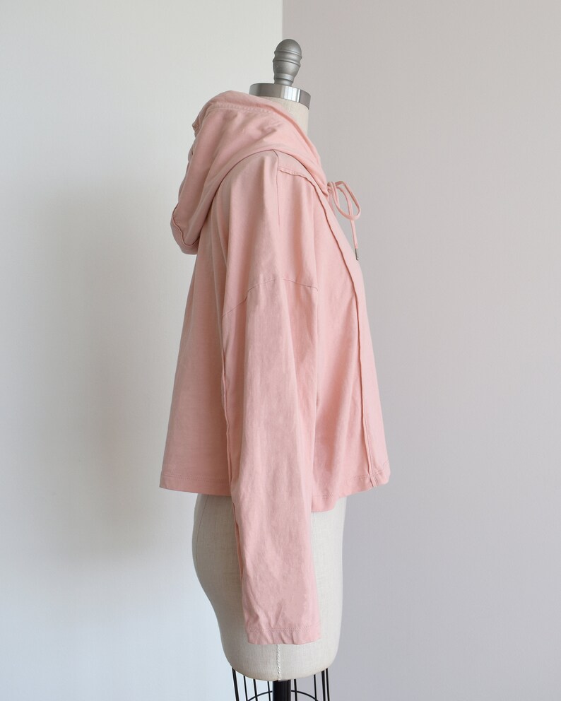 Light pink hoodie in lightweight t-shirt cotton, tonal piping along sleeves and chest, drawstring with silver endings