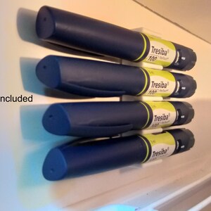 May include: Four blue insulin pens are stored in a white refrigerator door organizer. The pens are labeled "Tresiba" and are stored vertically. The organizer is attached to the refrigerator door with adhesive.