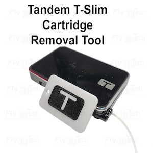 Könnte beinhalten: Ein schwarzes Tandem T-Slim-Gerät mit einem weißen und schwarzen Patronenentfernungswerkzeug. Das Werkzeug hat ein Schlüsselloch und ein großes weißes "T" auf schwarzem Hintergrund. Der Text "Tandem T-Slim Cartridge Removal Tool" steht oben.