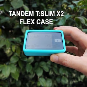 以下が含まれることがあります： Tandem T:Slim X2インスリンポンプ用の鮮やかなターコイズブルーの保護ケース。ケースは画面用の切り抜きがある長方形のフレームで、上部に「TANDEM T:SLIM X2 FLEX CASE」の文字が印刷されています。デバイスの画面には小さなTのロゴがあります。