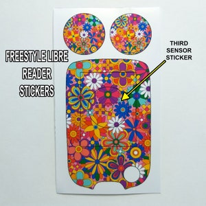 May include: A set of three colourful, floral patterned stickers for a Freestyle Libre reader and sensor. The reader sticker has a pink background with a variety of colourful flowers. The sensor sticker has a white background with a variety of colourful flowers. The text "FREESTYLE LIBRE READER STICKERS" is printed in black at the top of the image. The text "THIRD SENSOR STICKER" is printed in black at the top right of the image.